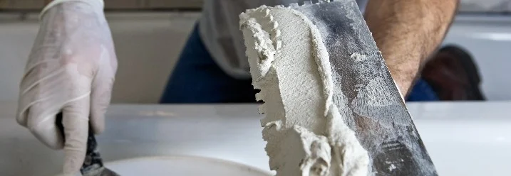 Person trägt Fliesenkleber mit Kelle auf